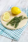 Lemon and rosemary on chopping board over wooden background — Stock Photo