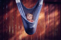 Boy lying in a hammock in front of wooden wall — Stock Photo