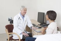 Médico hablando con paciente femenina en sala de examen - foto de stock