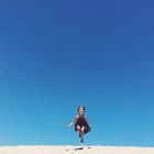Adorable niña saltando en la playa de arena contra el cielo azul - foto de stock