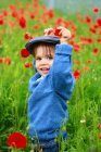 Kleiner Junge steht im Feld blühender Mohnblumen — Stockfoto