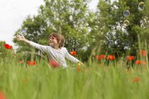 Boy playing with soap bubbles in a poppy field — Stock Photo