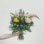 Female hand holding bouquet of beautiful flowers on grey background — Stock Photo