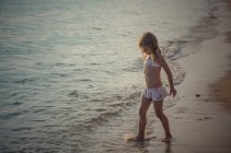 Girl standing and playing with water on sandy beach — Stock Photo