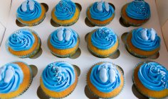 Box of cupcakes with blue cream and feet shape decoration — Stock Photo