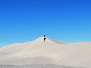 Женщина, занимающаяся йогой, позирует на песчаной дюне на фоне голубого неба — стоковое фото