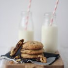Stack of chocolate cookies with bottles of milk over wooden background — Stock Photo