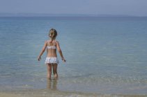 Bambina che indossa costume da bagno a piedi in mare — Foto stock
