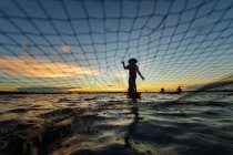 Silhueta de pescador em pé no barco e puxando a rede ao pôr do sol, Nongkhai, Tailândia — Fotografia de Stock