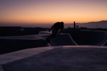 Silhouette of skateboarder on ramp at sunset with mountains on background — Stock Photo