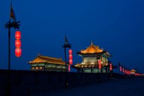 China, Shaanxi, Xian, Antigua muralla de la ciudad frente a los edificios tradicionales por la noche - foto de stock