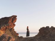 Жінка стоїть між скелями біля океану на заході сонця — стокове фото