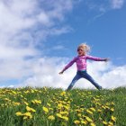 Mädchen springt in einem Feld von Löwenzahn mit bewölktem Himmel auf dem Hintergrund — Stockfoto