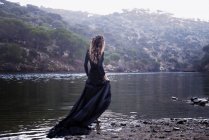 Mulher vestindo vestido preto andando na água na natureza — Fotografia de Stock