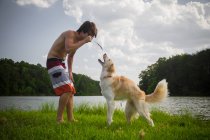 Молодой человек играет с собакой-колли на озере — стоковое фото
