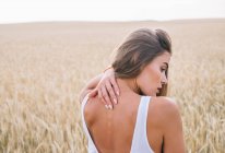Задний вид женщины, стоящей на пшеничном поле и касающейся спины — стоковое фото