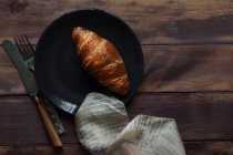 Vista superior de croissant en el plato, servilleta y utensilio de comer en la mesa de madera - foto de stock