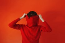 Чоловік тягне червоний светр на обличчя на червоному тлі — стокове фото