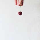 Human hand holding fresh cherry on white patterned background — Stock Photo