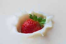 Gros plan des éclaboussures de fraises fraîches dans la crème — Photo de stock