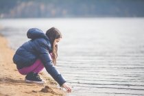 Girl crouching at lake and touching water — Stock Photo