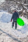 Menino andando na neve transportando trenó — Fotografia de Stock