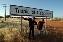 Adolescente y niña de pie bajo el signo de Trópico de Capricornio, Namibia - foto de stock