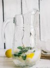 Glass pitcher with fresh lemonade lime, mint and ice cubes on wooden table — Stock Photo