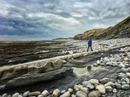 Garçon marchant le long de la plage rocheuse sous un ciel nuageux — Photo de stock