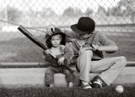Imagen monocromática de dos chicos caucásicos con bate de béisbol sentado en la cancha - foto de stock