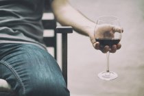 Обрізане зображення людини, що сидить на стільці, тримає келих червоного вина — стокове фото