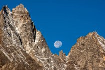 Himalaya, Kumbu, vista panorámica de la luna visible detrás de montañas rocosas en el cielo azul durante el día - foto de stock