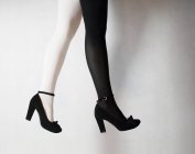 Cropped image of Woman legs with two colored tights, wearing black heels — Stock Photo