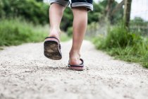 Vista posteriore delle gambe del bambino che camminano con le infradito — Foto stock