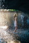 Жінка стоїть у водному фонтані на сонячному світлі — стокове фото