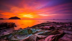 Vista panorámica de la puesta del sol y el cielo dramático sobre la playa rocosa - foto de stock