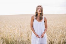Retrato de mulher bonita sensual em vestido branco em pé no campo de trigo e olhando para o espectador — Fotografia de Stock