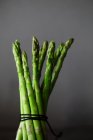 Bunch of tied asparagus spears against grey background — Stock Photo