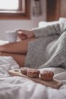 Imagem cortada de mulher atraente com pele bonita deitada na cama com xícara de café e bolos — Fotografia de Stock