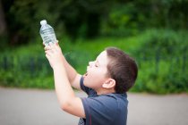 Мальчик пьет воду из отверстия на дне бутылки с водой — стоковое фото