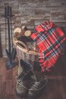 Walking Boots, blanket, hearth set and firewood in a basket — Stock Photo