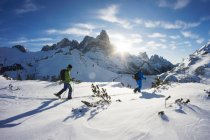 Vista lateral de dos valientes viajeros caminando en montañas nevadas con esquís - foto de stock