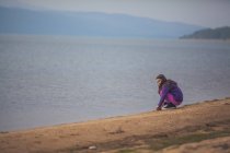 Menina agachado no lago na natureza com montanhas no fundo — Fotografia de Stock