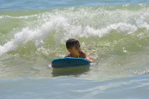 Мальчик плавает на доске для серфинга по волнам в океане — стоковое фото