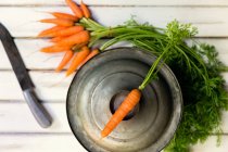 Вид сверху на кучу моркови, нож и кастрюлю на деревянном фоне — стоковое фото