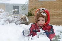 Маленький мальчик строит снеговика в саду — стоковое фото