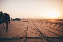 Silueta de dos surfistas y coche en la playa al amanecer, namibia - foto de stock