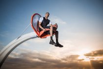 Portrait of a young man sitting in a basketball hoop in a park — Stock Photo