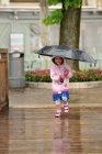 Mädchen im Regenmantel hält Regenschirm auf Holzweg — Stockfoto