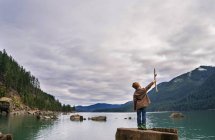 Boy standing on rocks at river and holding stick — Stock Photo